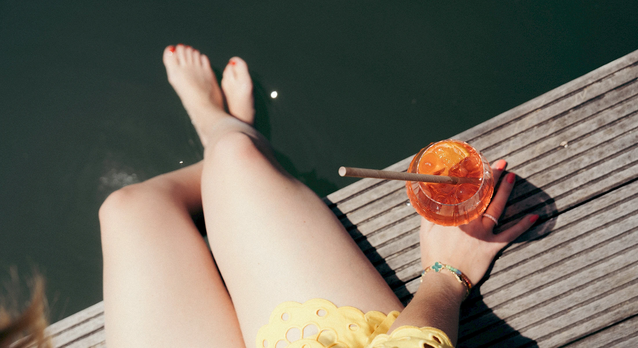 Frau sitzt mit Drink am Schliersee und lässt ihre Beine ins Wasser hängen