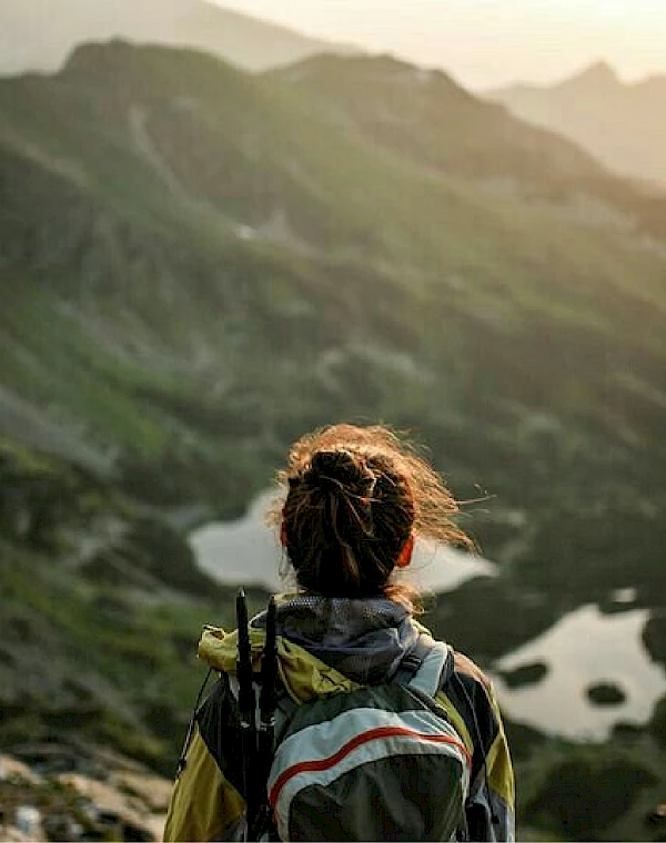 Wanderin blickt in sanftem Sonnenlicht auf ruhige Bergseen und schöne Bergsilhouetten